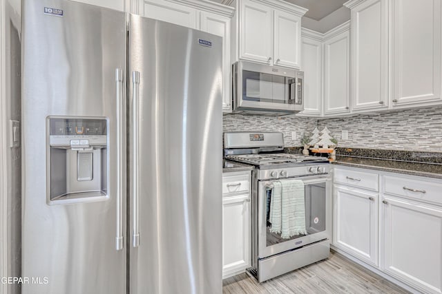 kitchen featuring dark stone counters, light hardwood / wood-style floors, decorative backsplash, white cabinets, and appliances with stainless steel finishes