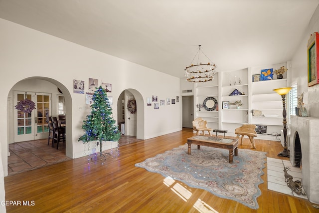 living room with a tile fireplace, an inviting chandelier, french doors, hardwood / wood-style flooring, and built in shelves