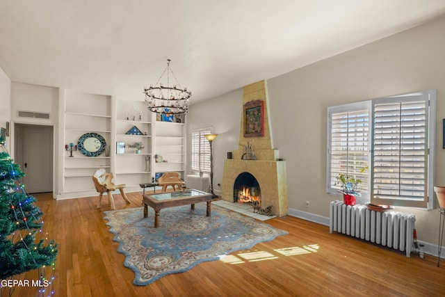 living room with hardwood / wood-style floors, a large fireplace, radiator, and a chandelier