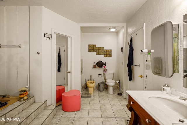 bathroom with tile patterned flooring, a bidet, a textured ceiling, toilet, and vanity