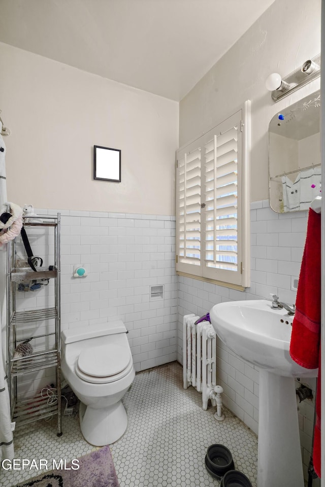 bathroom with tile patterned flooring, toilet, radiator, and tile walls