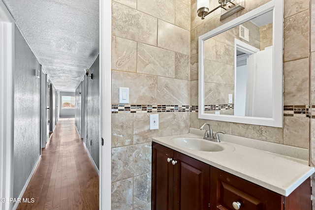 bathroom featuring vanity, a textured ceiling, hardwood / wood-style flooring, and tile walls