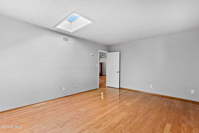 spare room featuring a skylight and light hardwood / wood-style floors