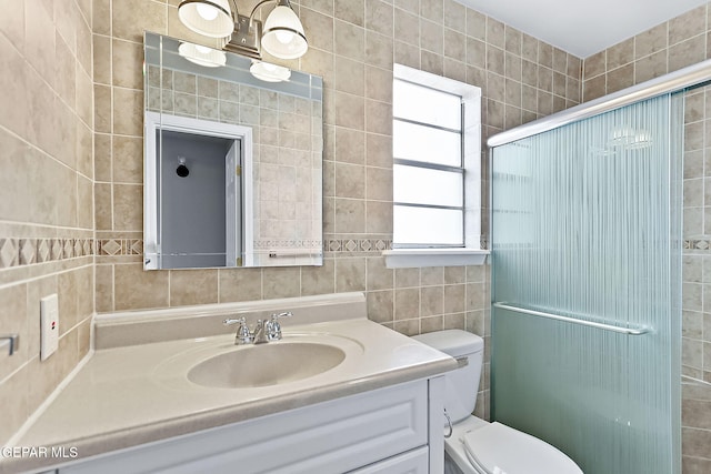 bathroom with vanity, toilet, a shower with shower door, and tile walls