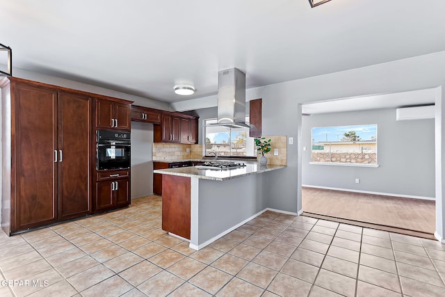 kitchen with island exhaust hood, kitchen peninsula, light stone countertops, an AC wall unit, and black oven