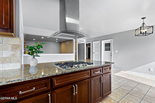 kitchen featuring island exhaust hood, light stone countertops, stainless steel gas cooktop, light tile patterned floors, and an inviting chandelier