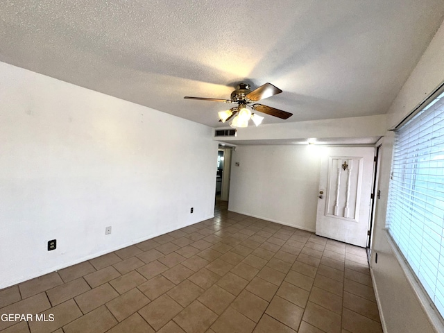 tiled empty room with ceiling fan and a textured ceiling