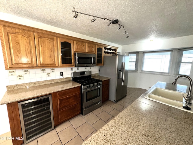 kitchen with appliances with stainless steel finishes, sink, wine cooler, light tile patterned floors, and light stone counters