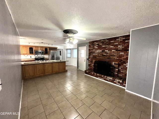 kitchen with rail lighting, ceiling fan, appliances with stainless steel finishes, a textured ceiling, and a brick fireplace