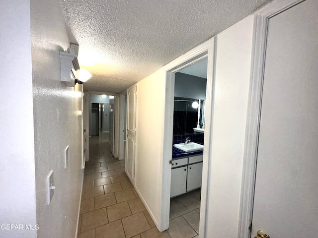 hall featuring light tile patterned flooring, sink, and a textured ceiling