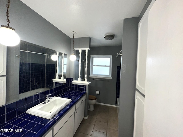 bathroom with toilet, a tile shower, vanity, tile patterned flooring, and backsplash