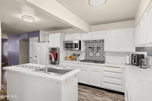 kitchen featuring tile countertops, dark wood-type flooring, sink, appliances with stainless steel finishes, and white cabinetry