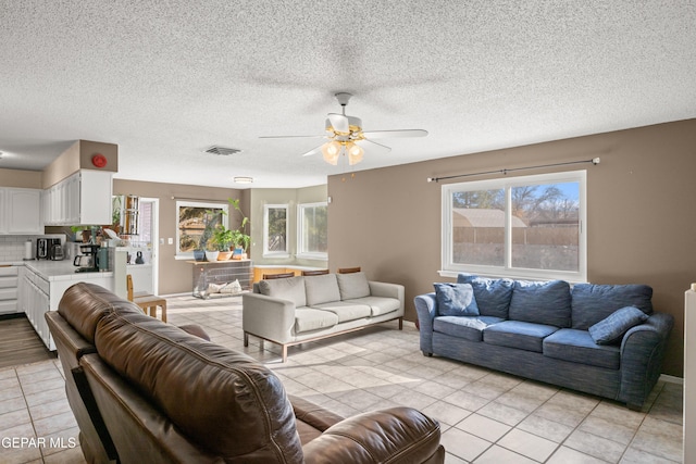 living room featuring ceiling fan, plenty of natural light, light tile patterned flooring, and a textured ceiling