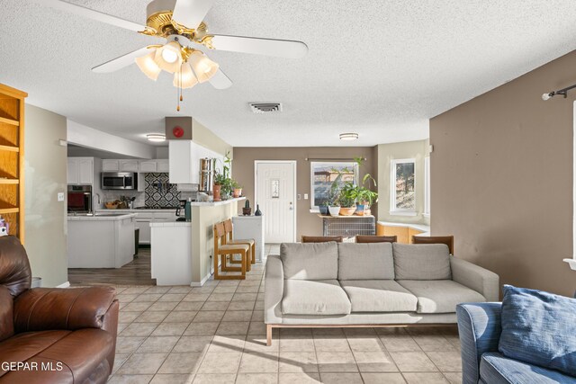 tiled living room featuring ceiling fan, sink, and a textured ceiling