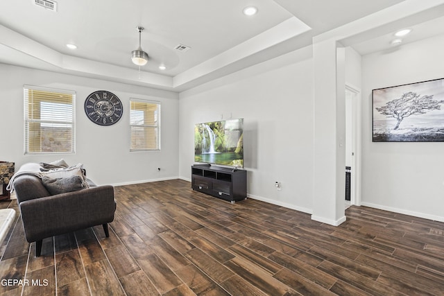 living room with dark hardwood / wood-style floors, ceiling fan, and a tray ceiling