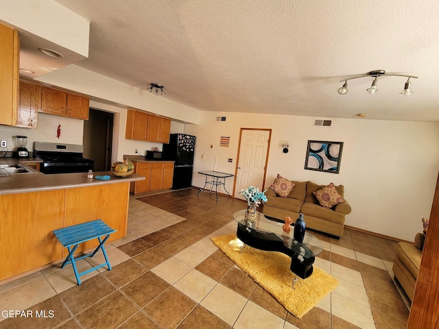 kitchen with kitchen peninsula, gas range, black refrigerator, and a textured ceiling