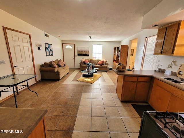 kitchen featuring stove, a textured ceiling, light tile patterned floors, and sink