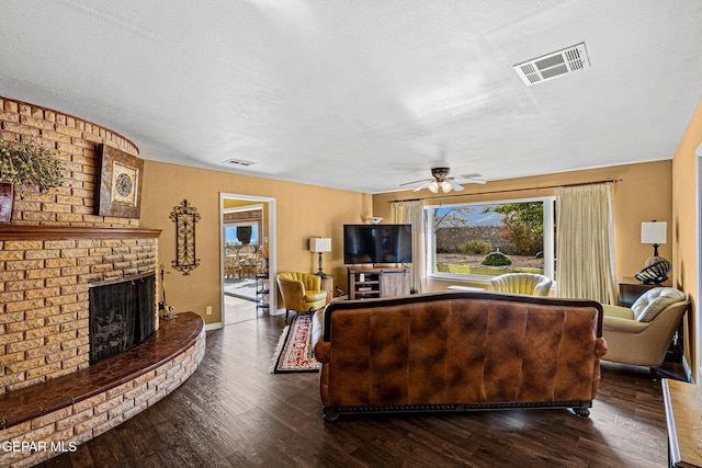 living room featuring a brick fireplace, dark wood-type flooring, a textured ceiling, and ceiling fan