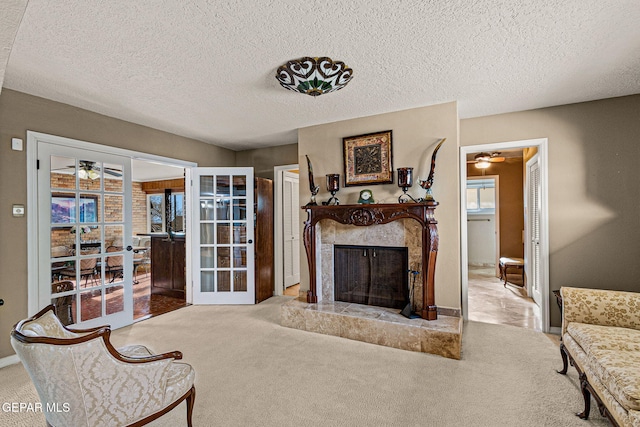 carpeted living room featuring ceiling fan, a premium fireplace, french doors, and a textured ceiling