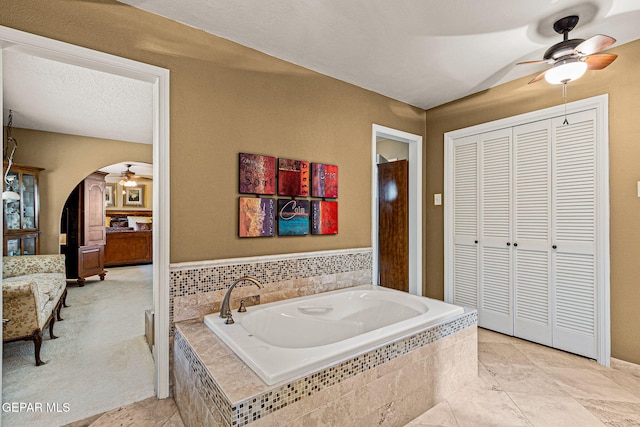 bathroom with tiled tub, a textured ceiling, and ceiling fan