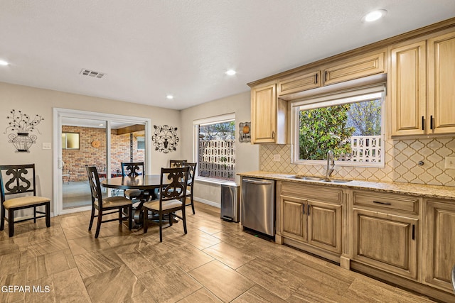 kitchen featuring tasteful backsplash, dishwasher, light stone countertops, and sink