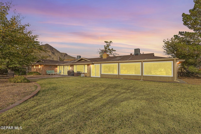 back house at dusk featuring cooling unit and a lawn