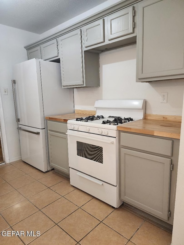 kitchen featuring butcher block countertops, gray cabinetry, light tile patterned floors, and white appliances