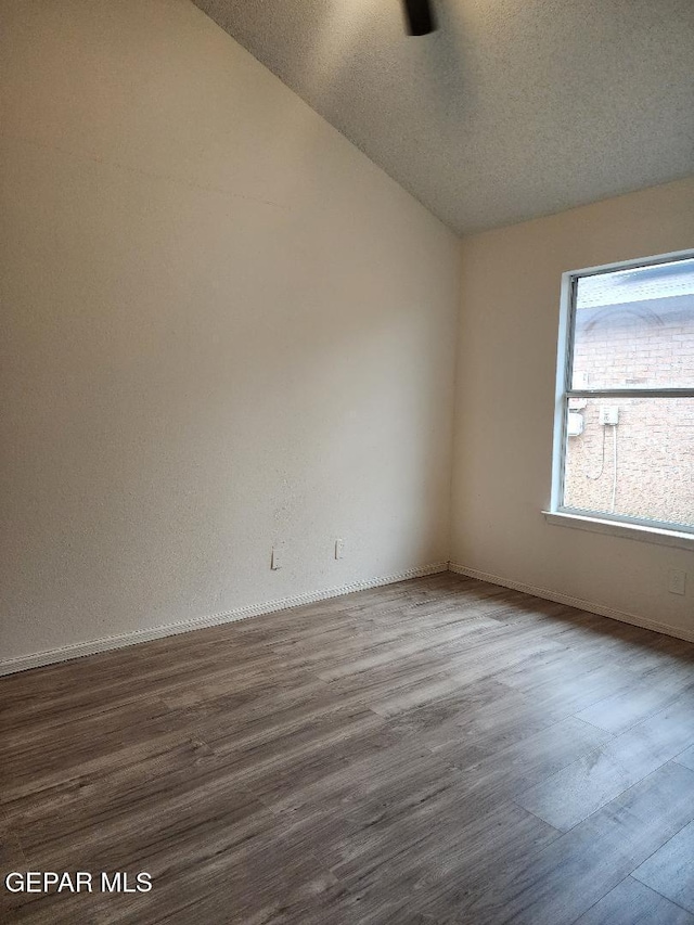 spare room with wood-type flooring, a textured ceiling, and lofted ceiling