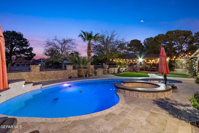 pool at dusk with an in ground hot tub and a patio