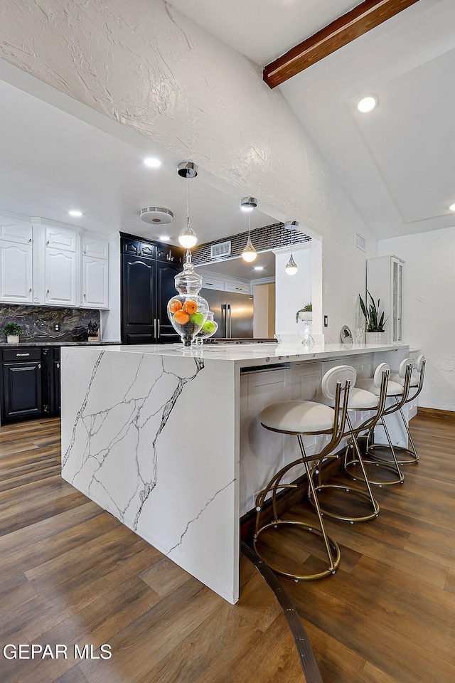 11179 Leo Collins Dr, El Paso, TX 79936 - kitchen featuring a breakfast bar area, tasteful backsplash, light stone counters, white cabinetry, and dark wood-type flooring