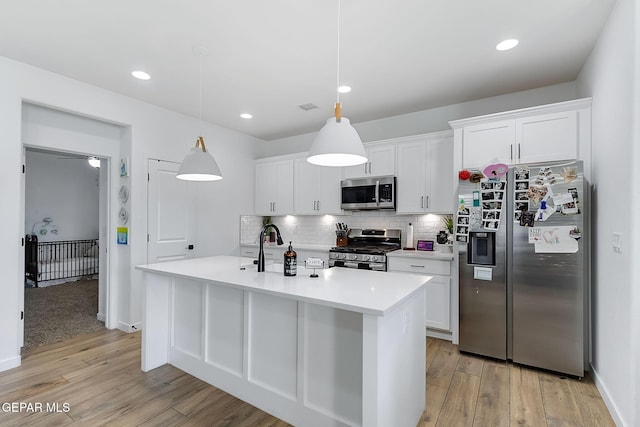 kitchen featuring stainless steel appliances, white cabinetry, an island with sink, and decorative light fixtures