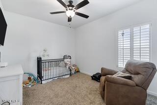 carpeted bedroom with a nursery area and ceiling fan