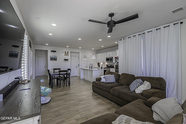 living room featuring ceiling fan, sink, and light hardwood / wood-style floors