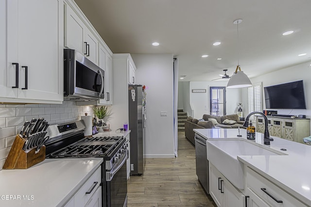 kitchen with appliances with stainless steel finishes, decorative light fixtures, tasteful backsplash, white cabinetry, and light hardwood / wood-style floors