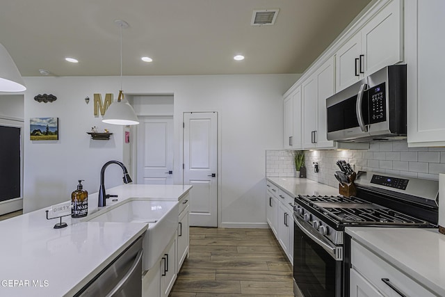 kitchen featuring white cabinetry, decorative light fixtures, dark hardwood / wood-style floors, stainless steel appliances, and backsplash