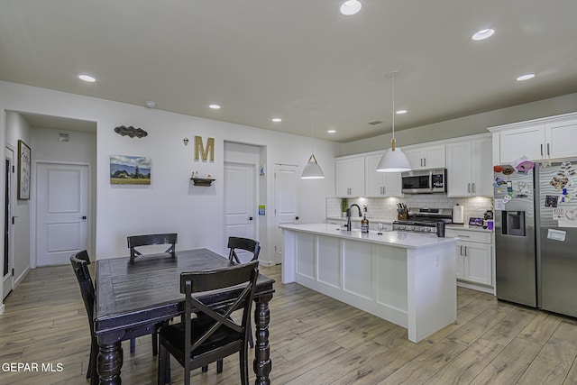 kitchen featuring appliances with stainless steel finishes, a kitchen island with sink, hanging light fixtures, tasteful backsplash, and white cabinets