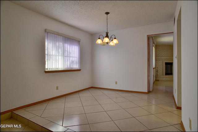 spare room with a fireplace, light tile patterned floors, a textured ceiling, and an inviting chandelier