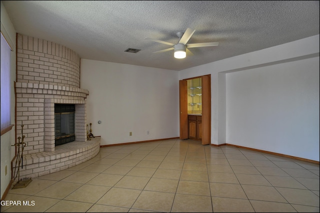 unfurnished living room featuring ceiling fan, light tile patterned floors, a textured ceiling, and a brick fireplace