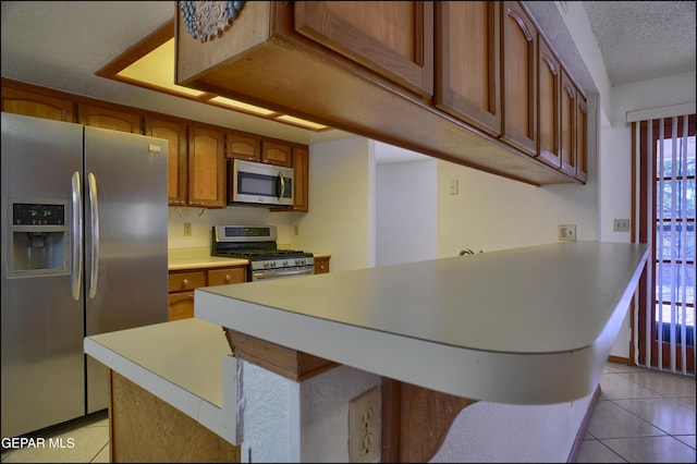 kitchen featuring a breakfast bar, appliances with stainless steel finishes, a textured ceiling, and light tile patterned floors