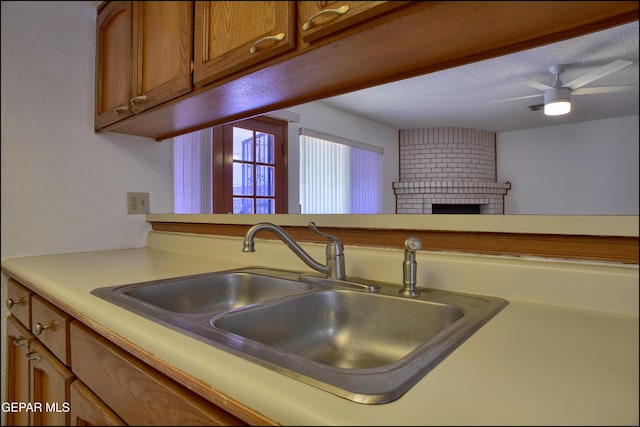 kitchen featuring a textured ceiling, a brick fireplace, ceiling fan, and sink