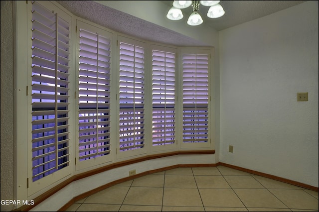 tiled empty room with a textured ceiling and a notable chandelier