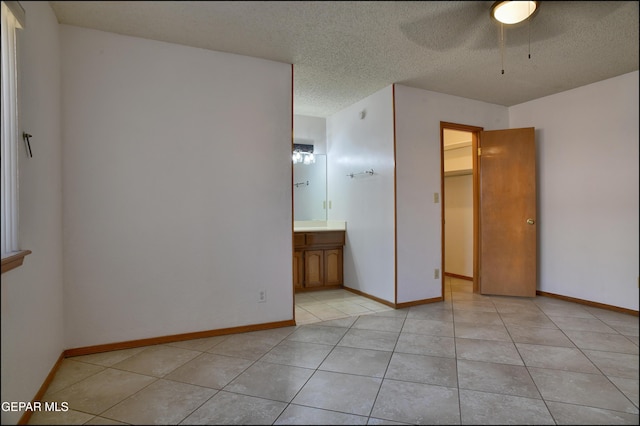 unfurnished bedroom with ensuite bathroom, a textured ceiling, light tile patterned floors, a spacious closet, and a closet