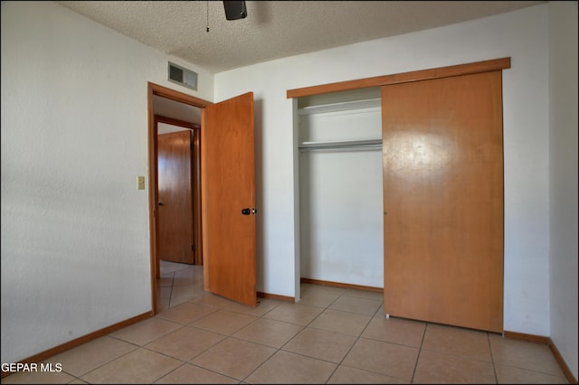 unfurnished bedroom featuring light tile patterned flooring, a textured ceiling, a closet, and ceiling fan