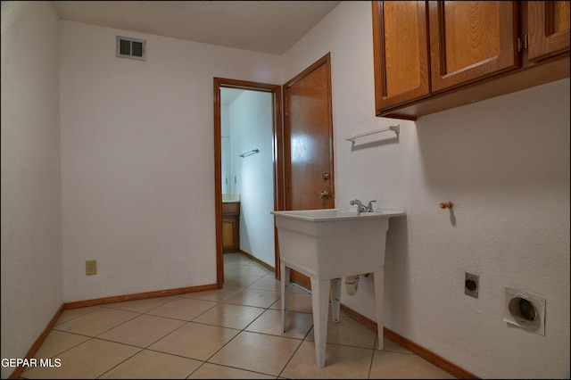 laundry area with electric dryer hookup, cabinets, and light tile patterned floors