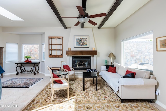 living room with beamed ceiling, ceiling fan, a large fireplace, and a skylight