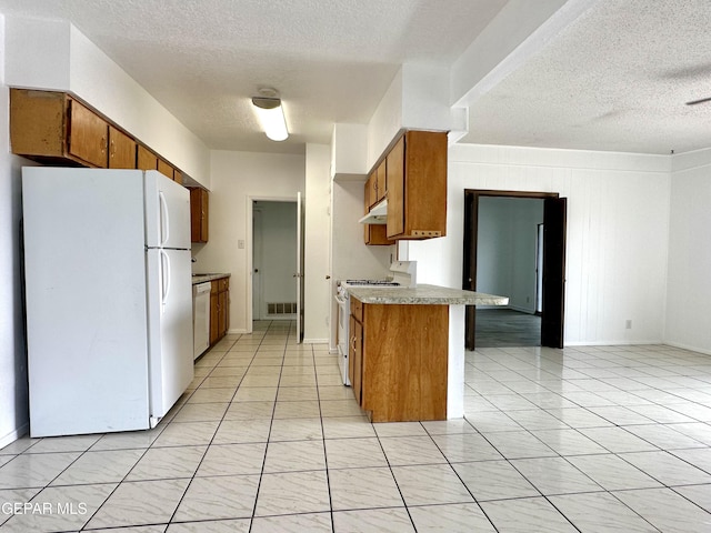 kitchen with kitchen peninsula, wood walls, a textured ceiling, white appliances, and light tile patterned floors