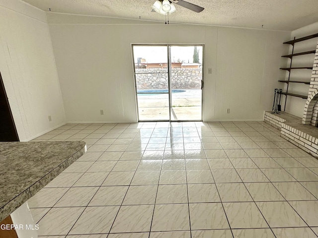 unfurnished living room with ceiling fan, light tile patterned floors, a textured ceiling, and a brick fireplace