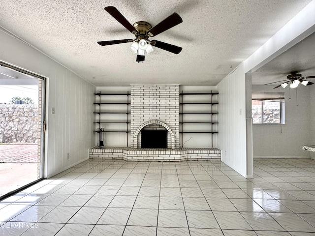 unfurnished living room with plenty of natural light, ceiling fan, a textured ceiling, and a brick fireplace