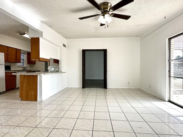 kitchen with ceiling fan, white refrigerator, kitchen peninsula, a textured ceiling, and light tile patterned flooring