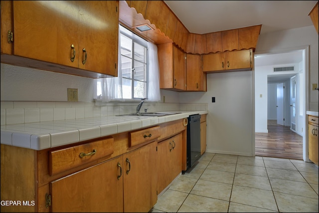 kitchen with dishwasher, light tile patterned floors, tile counters, and sink